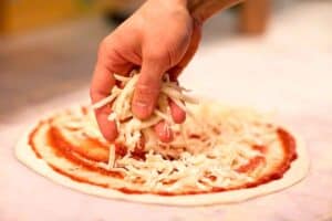 Preparing a grated cheese pizza.