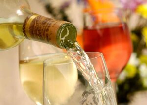 White wine being poured from a bottle into a glass, with other wine glasses softly blurred in the background.