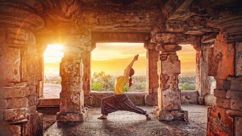A woman doing yoga at the Hampi temple at sunrise in India.