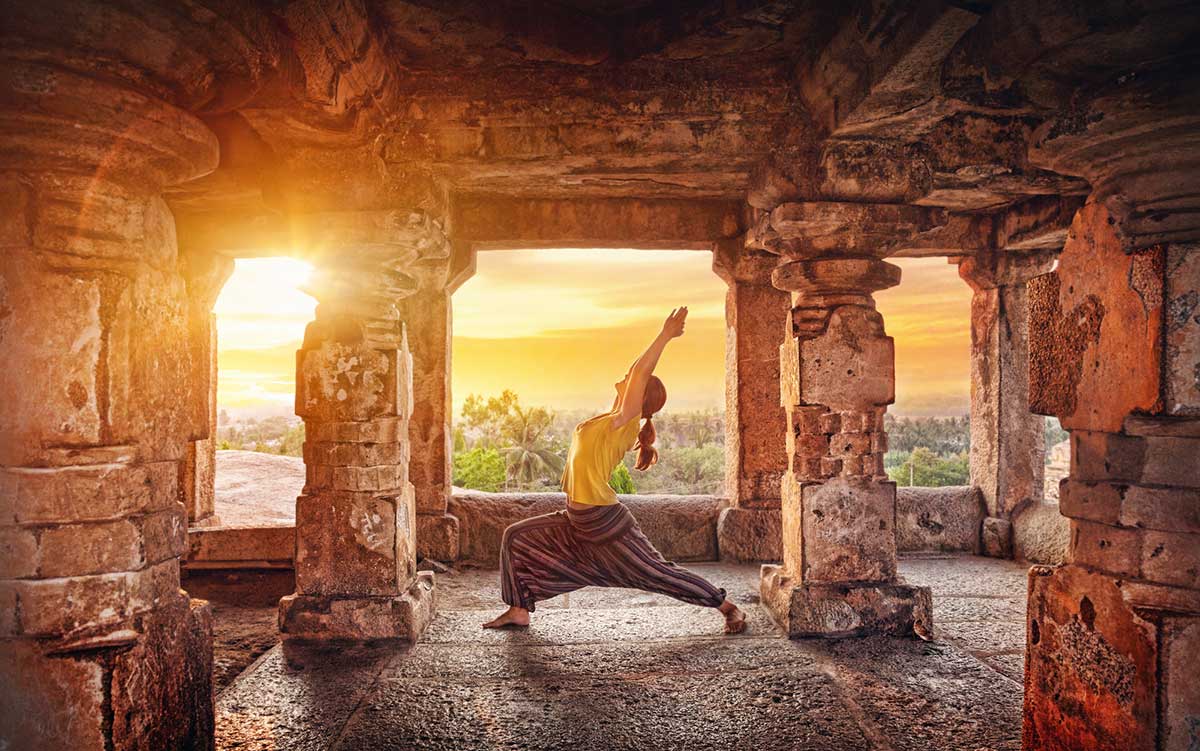 A woman doing yoga at the Hampi temple at sunrise in India.