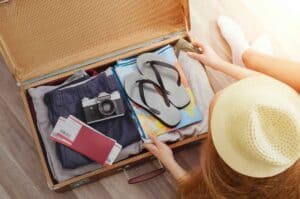 Young woman in hat sitting on wooden floor with open travel bag.