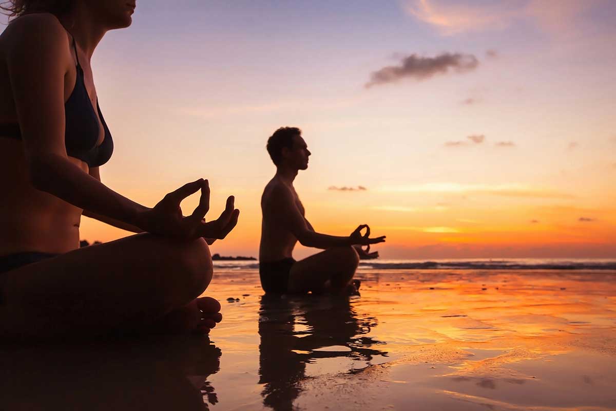 A man and a woman meditating on a beach in Mexico during sunset.
