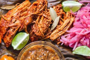 Cochinita pibil, Mexican pit-roasted pork dish from Yucatan peninsula, served on banana leaves with traditional condiments.
