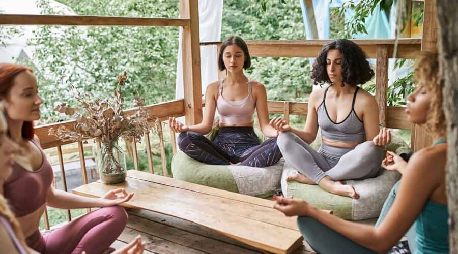 Group of women meditating in lotus pose in patio of retreat center in the Caribbean.