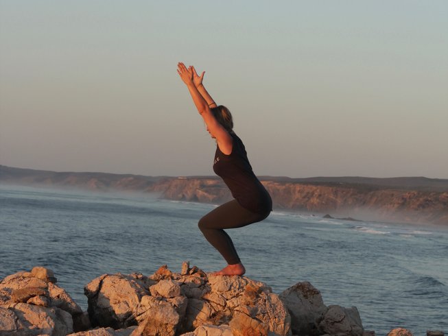 woman doing chair pose while standing on a rock