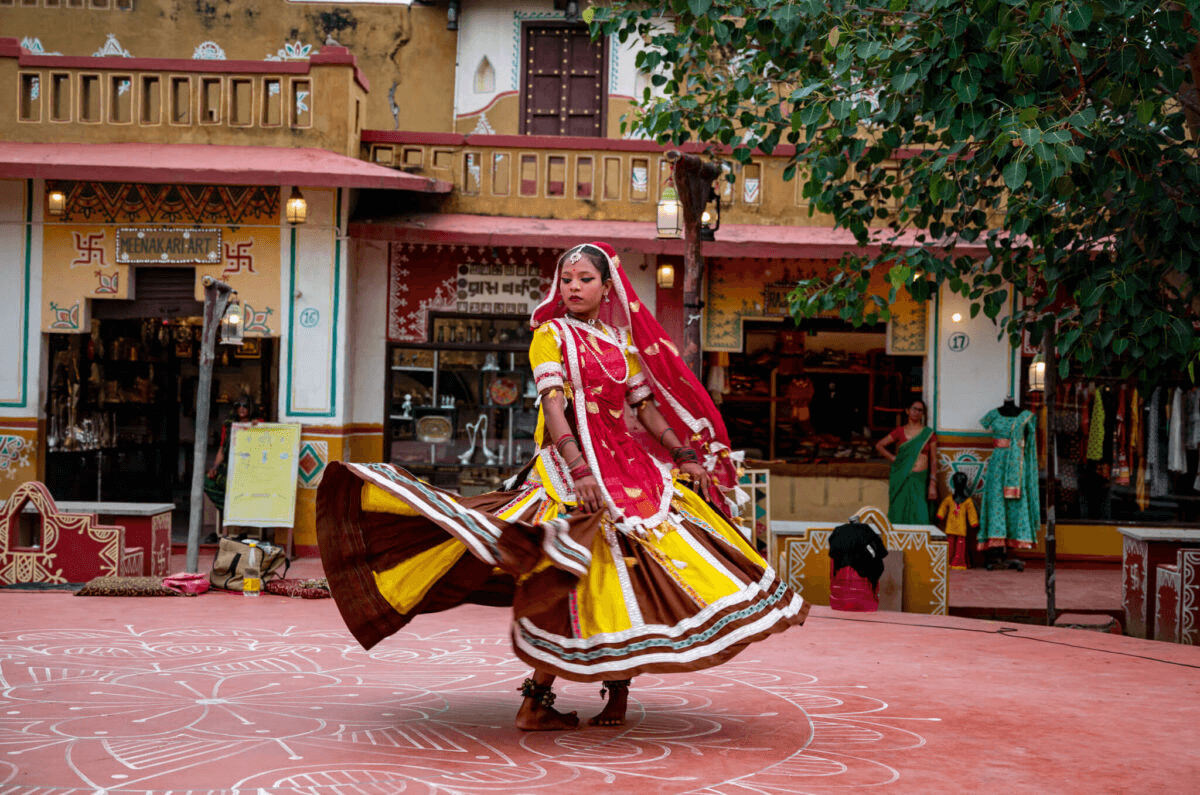 Rajasthani dancer performing in traditional colorful attire at Chokhi Dhani cultural village in Jaipur, India, surrounded by hand-painted decor and artisan shops.