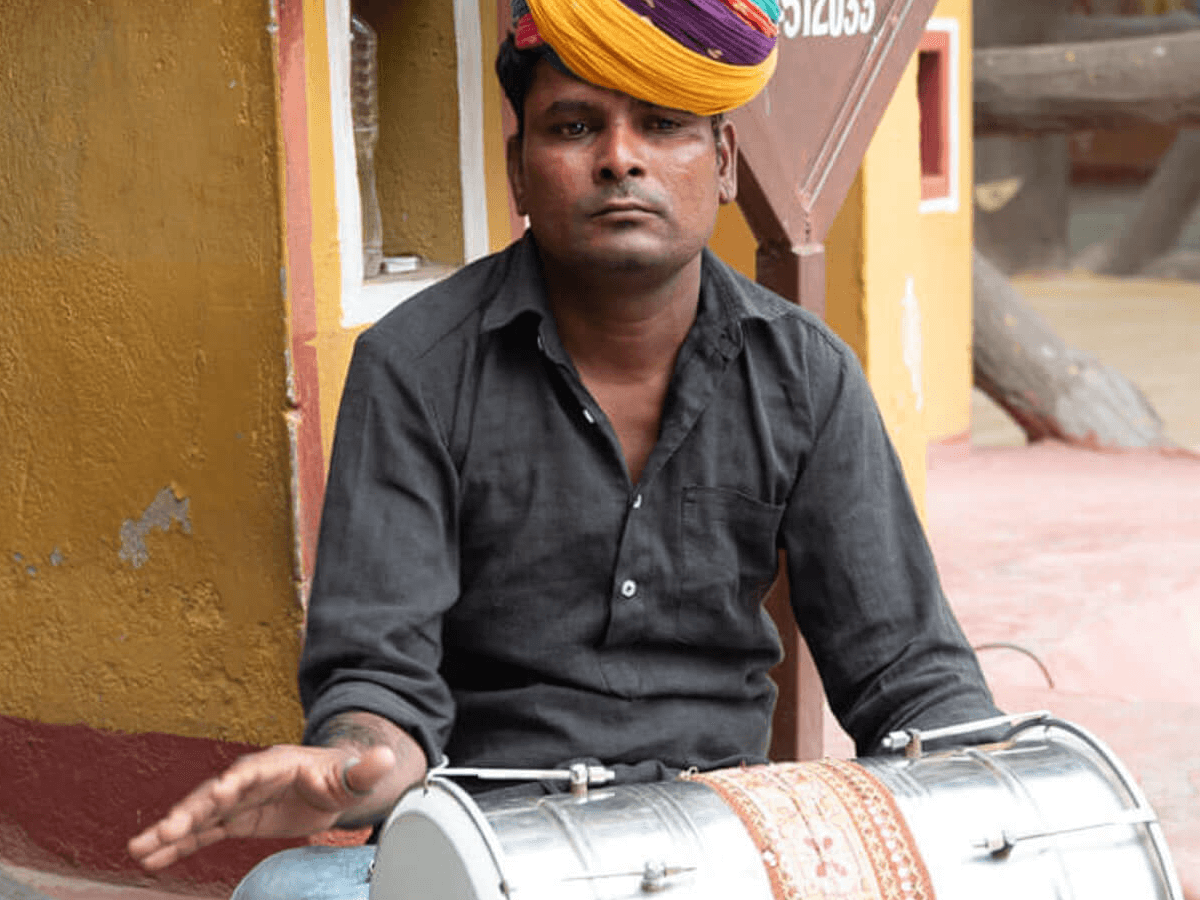 Traditional musician at Chokhi Dhani Village in Jaipur, India, playing a dhol drum while wearing a colorful Rajasthani turban—part of the cultural performances at the heritage-themed resort.