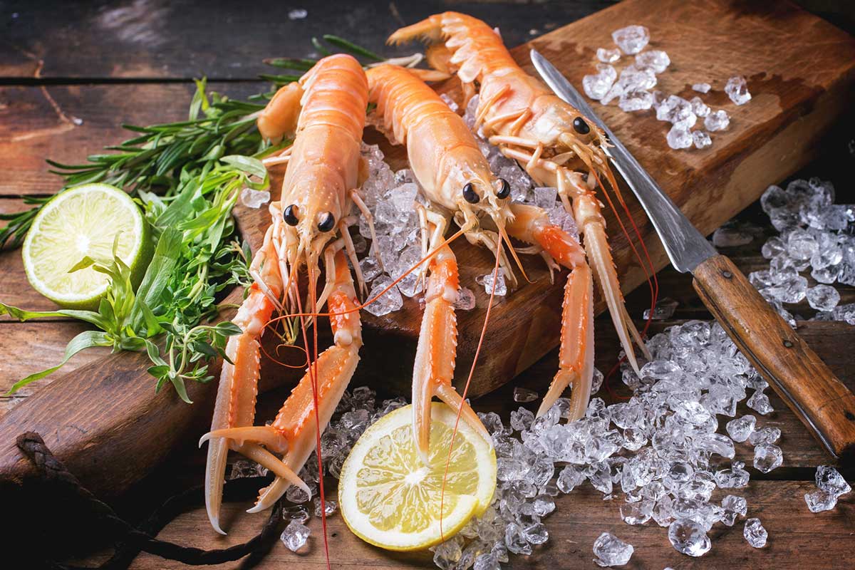 Fresh langoustines on a wooden chopping board with half lemon and ice.