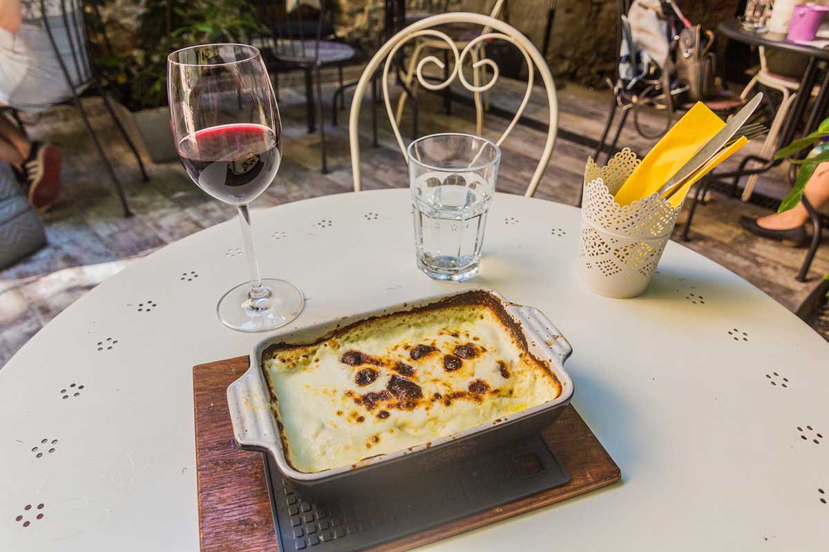 Photo of a traditional Croatian dish next to a glass of wine and water in a restaurant.
