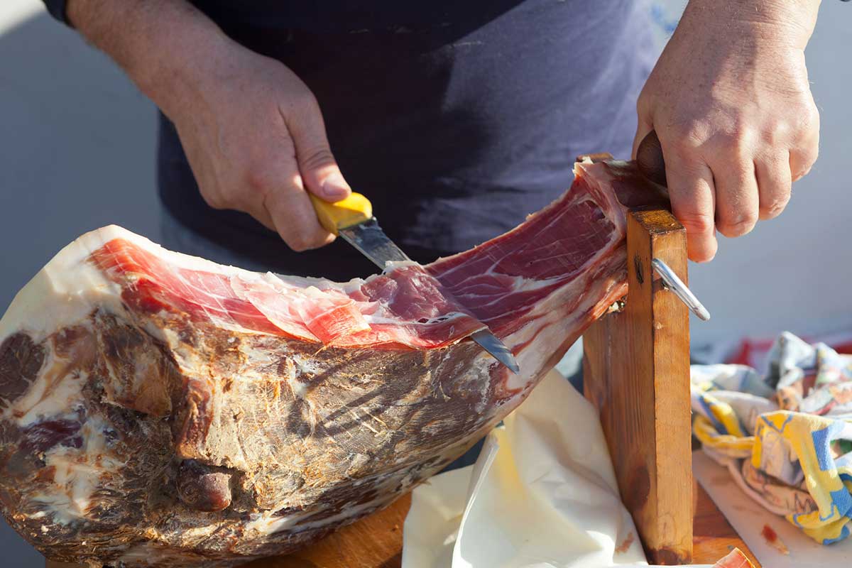 A close up photo of a man slicing Dalmatian prosciutto.