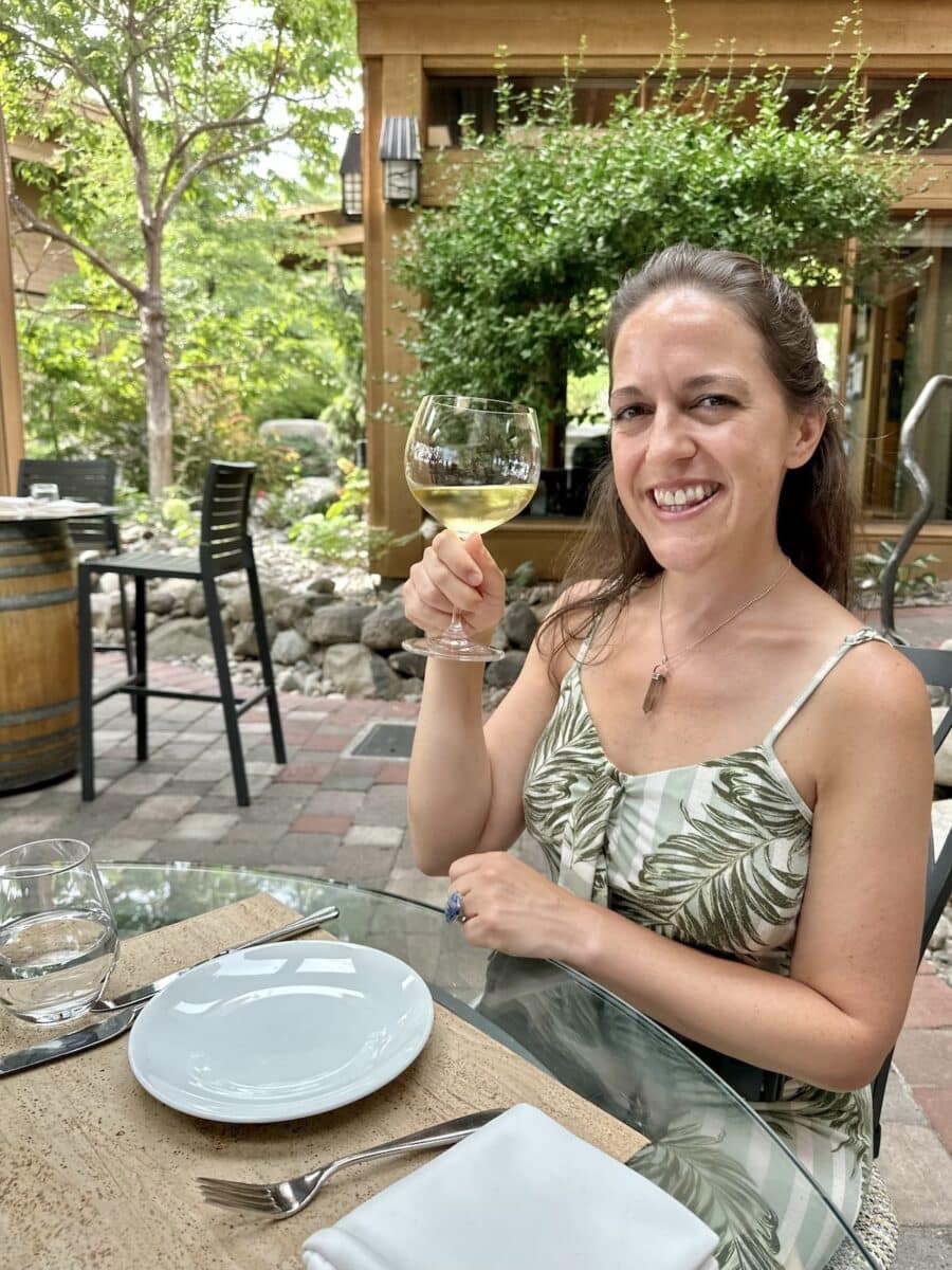 Woman in a green dress holding a glass of Chardonnay while dining at Old Vines Restaurant at Quails’ Gate Winery in British Columbia’s Okanagan Valley