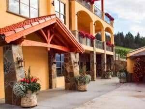 Exterior of Gray Monk Estate Winery in Lake Country, BC, with stone pillars, balconies, and colorful flowers overlooking the vineyards.