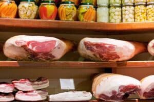 A close up photo of shelves with parma ham, bacon and pickles in Bologna Market.