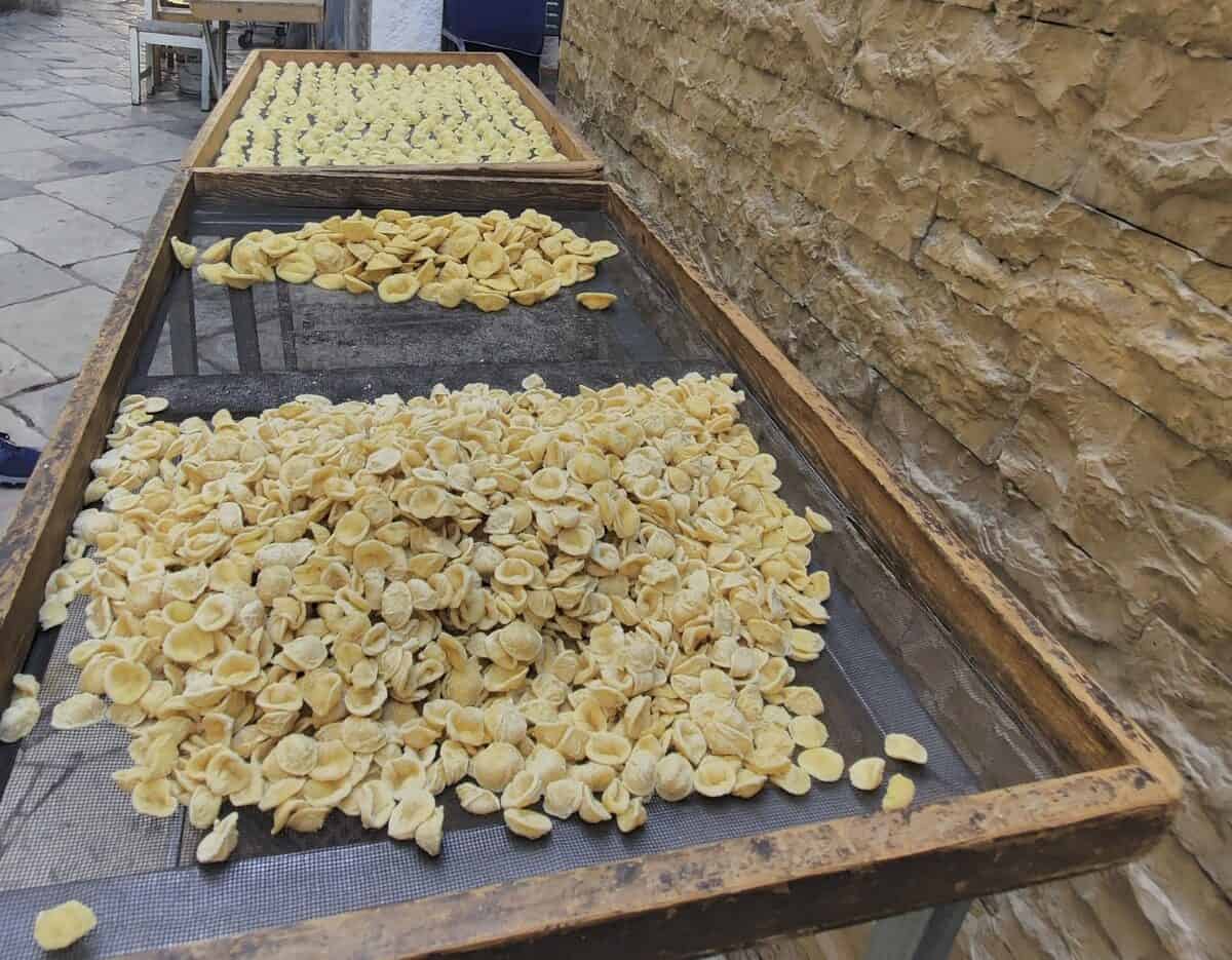 Freshly made orecchiette drying on large wooden mesh trays along a stone wall in Bari’s Old Town, part of the traditional pasta-making process on Strada delle Orecchiette.